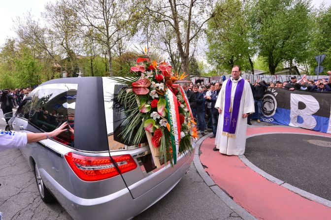 Priest Luciano Manenti watches the hearse carrying the coffin leaving after the funeral service.