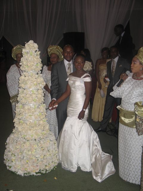 A Nigerian couple cut their wedding cake, surrounded by guests in traditional attire.