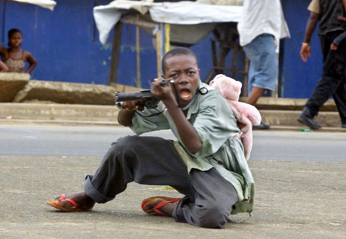 A child soldier wearing a teddy bear backpack points his gun at a photographer in a street of Monrovia in June 2003.