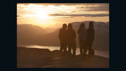 A group look out to the midnight sun on top of Mount Nuolja 