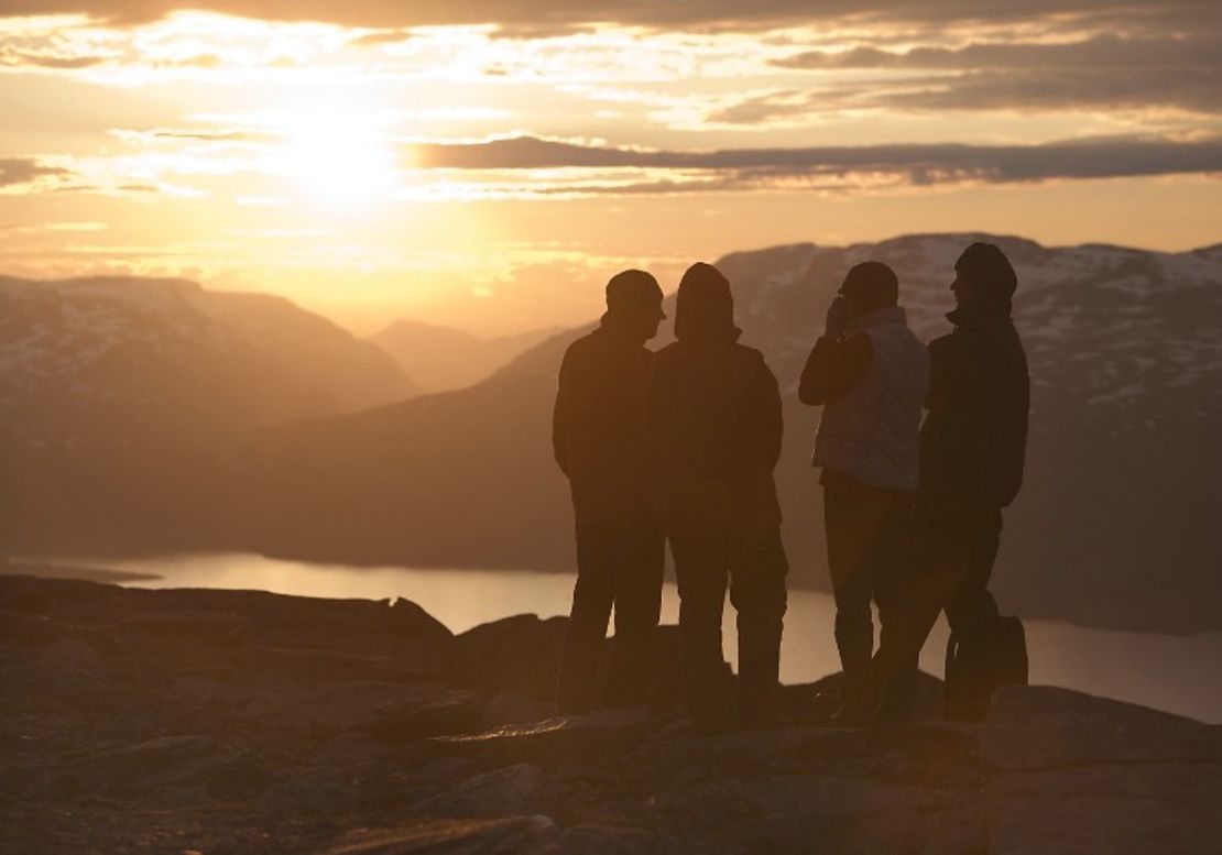 A group look out to the midnight sun on top of Mount Nuolja 