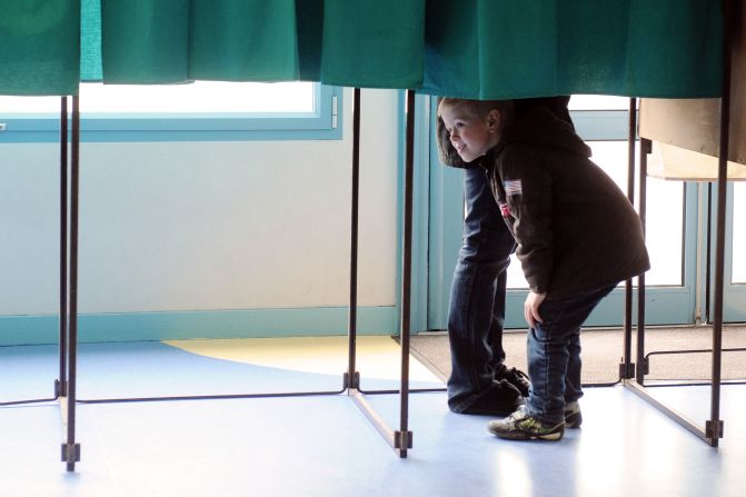 A child looks under the curtain of a voting booth in Henin-Beaumont, France, near the border with Belgium.