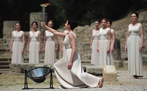 Amid the tumbledown columns and olive groves of the ancient stadium in Olympia, the high priestess holds the torch high at the lighting ceremony.