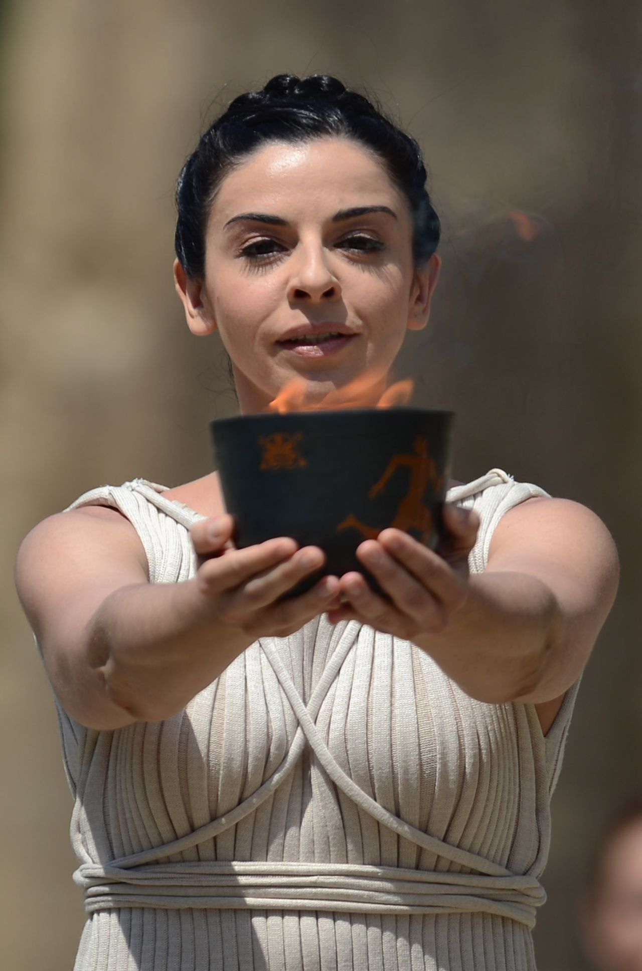 The priestess, played by Greek actress Ino Menegaki, lifts the "Archaic Pot" from which the flame is lit. 