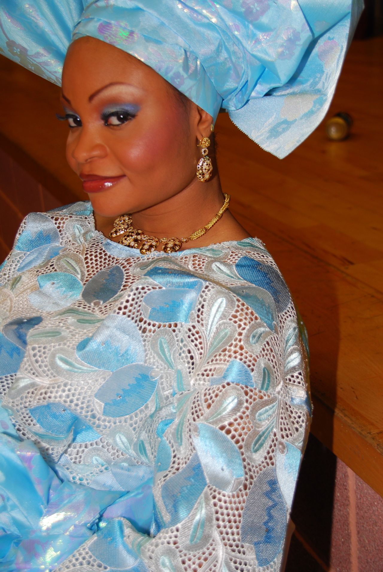 A bride wears bold-colored ancestral robes with embroidered detailing around the neckline and traditional Nigerian gele headdress. 