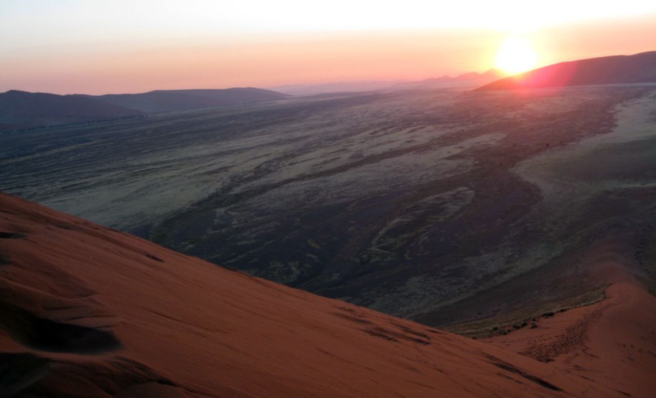 The sun rising over the dunes highlights the orange-red terrain.