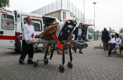 A rescuer pushes an elderly woman on a stretcher at the sports center of Finale Emilia.