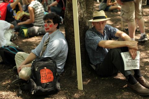 Two men rest against a tree before the start of protests on the first day of the NATO summit.