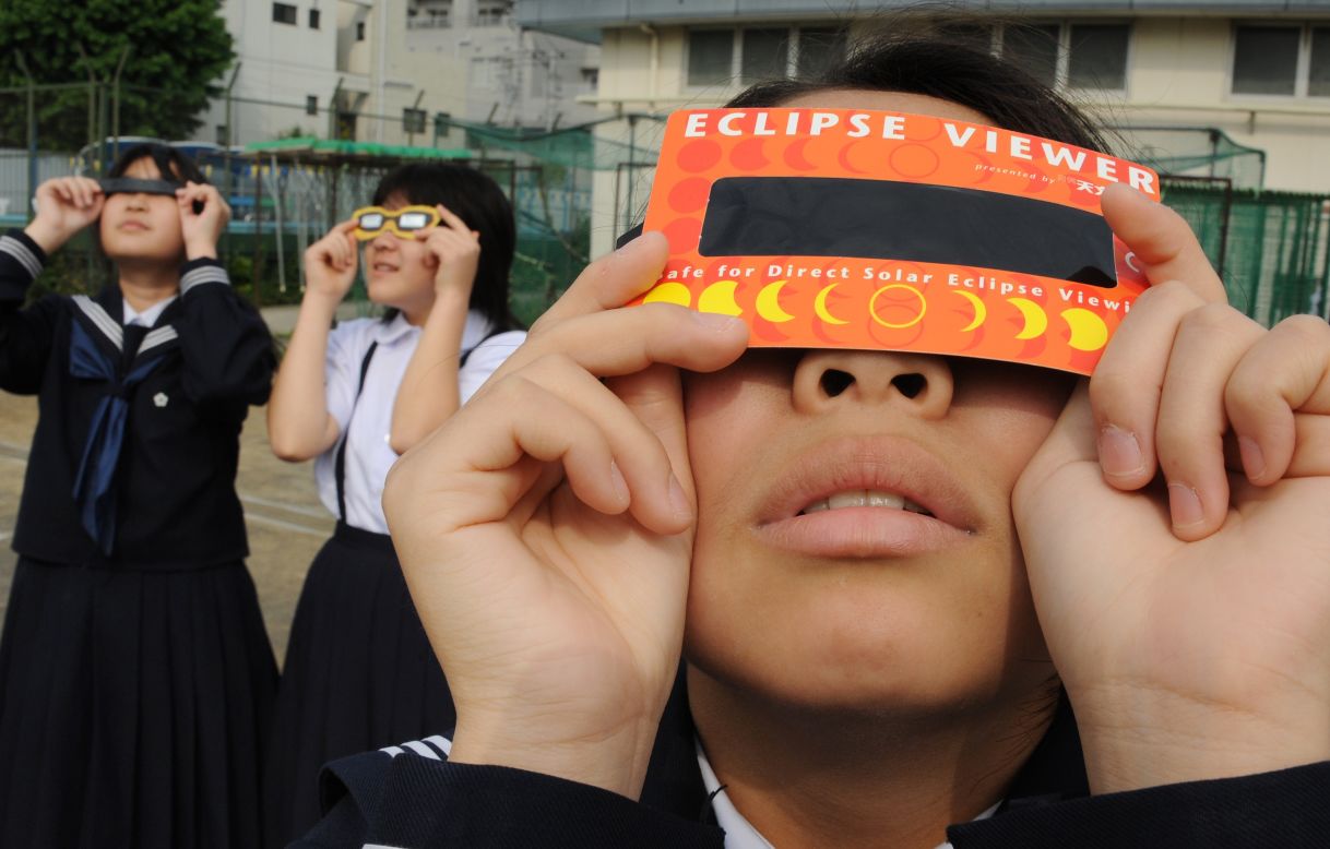 Junior high school students observe the solar eclipse through special glasses on a playground in Tokyo.