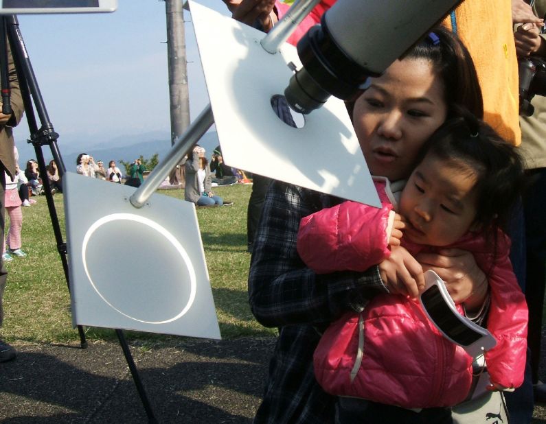 A girl and her mother observe the eclipse as it's projected onto a white background through a telescope in Tokyo.