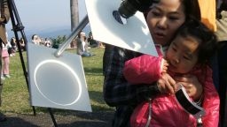 A girl and her mother observe the eclipse as it's projected onto a white background through a telescope in Tokyo.