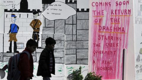 Schoolchildren walk past drawings and a slogan on a wall in the center of Athens in February.