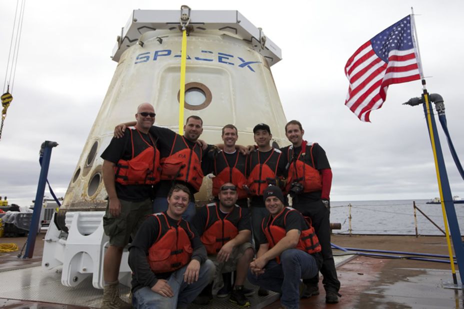 Dragon's recovery team poses in front of the first commercial capsule to reach orbit and return safely to Earth.
