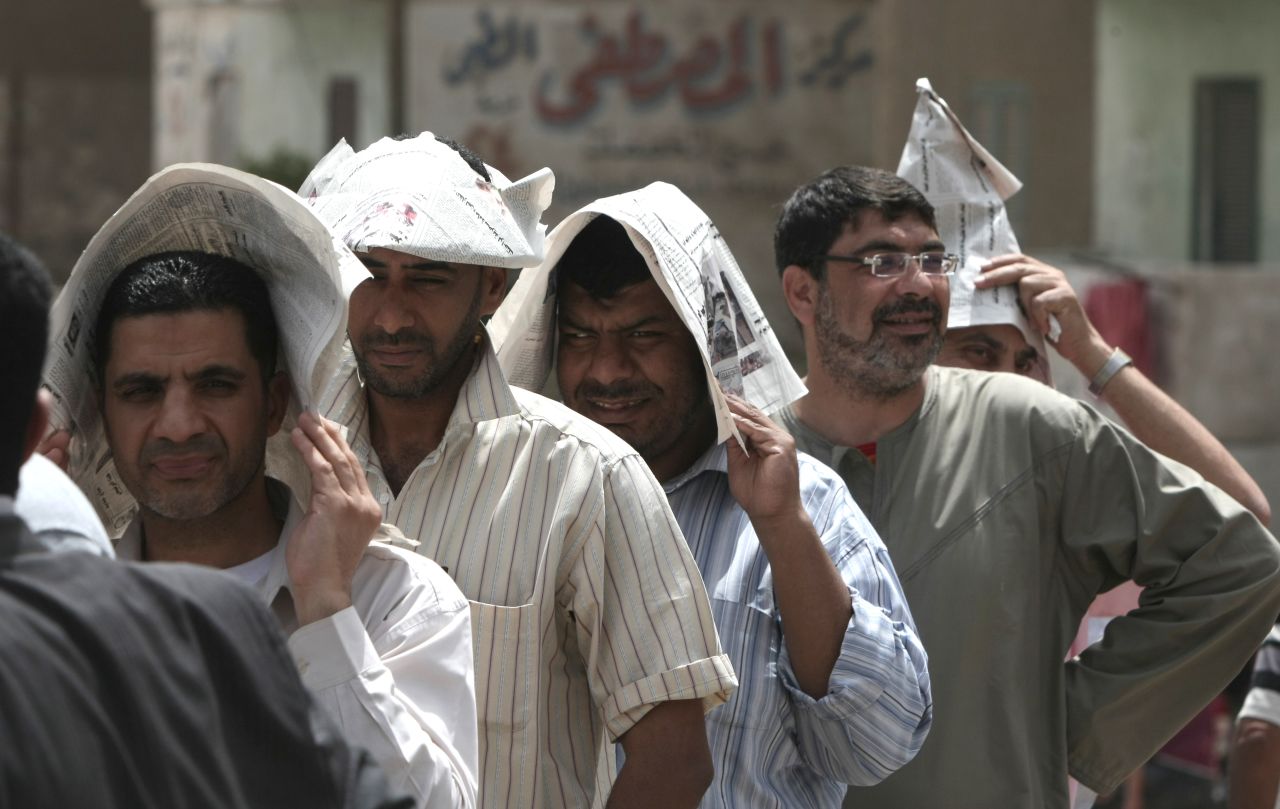Egyptian men shield themselves from the hot sun outside a Cairo polling station Wednesday.