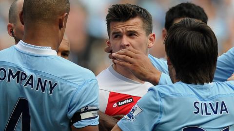 QPR midfielder Joey Barton (c) is surrounded by Manchester City players after kicking out at striker Sergio Aguero