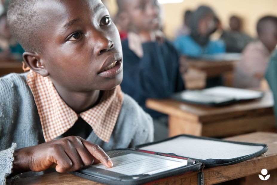 A young Masai boy listens to his teacher as he follows the lesson in a Kenyan textbook on his e-reader.