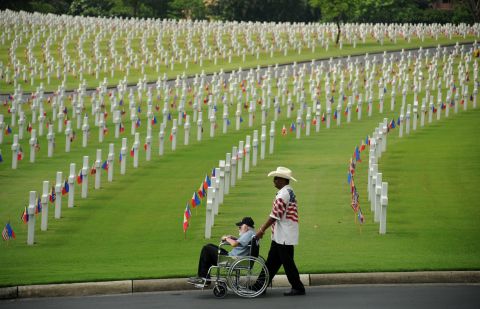A man pushes an elderly man past the graves Sunday at the Manila American Cemetery.