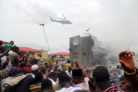 A helicopter hovers over the neighborhood in Lagos. Throngs of people flocked to the area despite debris, fires and thick smoke.