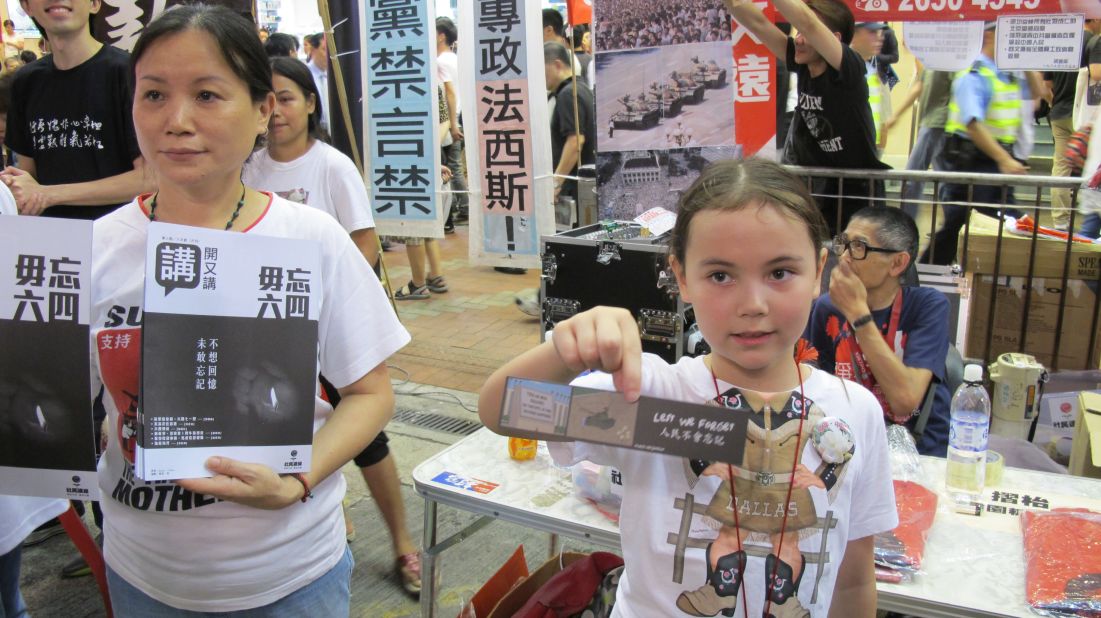Volunteer Nicole Lai, 7, hands out bookmarks to passersby at the League of Social Democrats booth alongside her mother (L).  "Many people died so I'm here to pay my respects," she says.