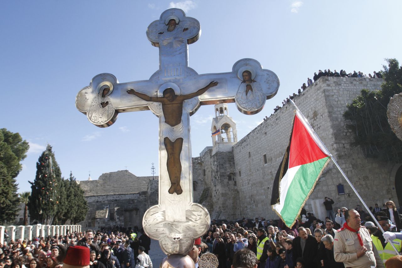 A cross held aloft in Manger Square, next to a Palestinian flag. One of Christianity's holiest sites, the Church of the Nativity is one of the biggest tourist destinations in the Palestinian territories, and drew about two million visitors last year.