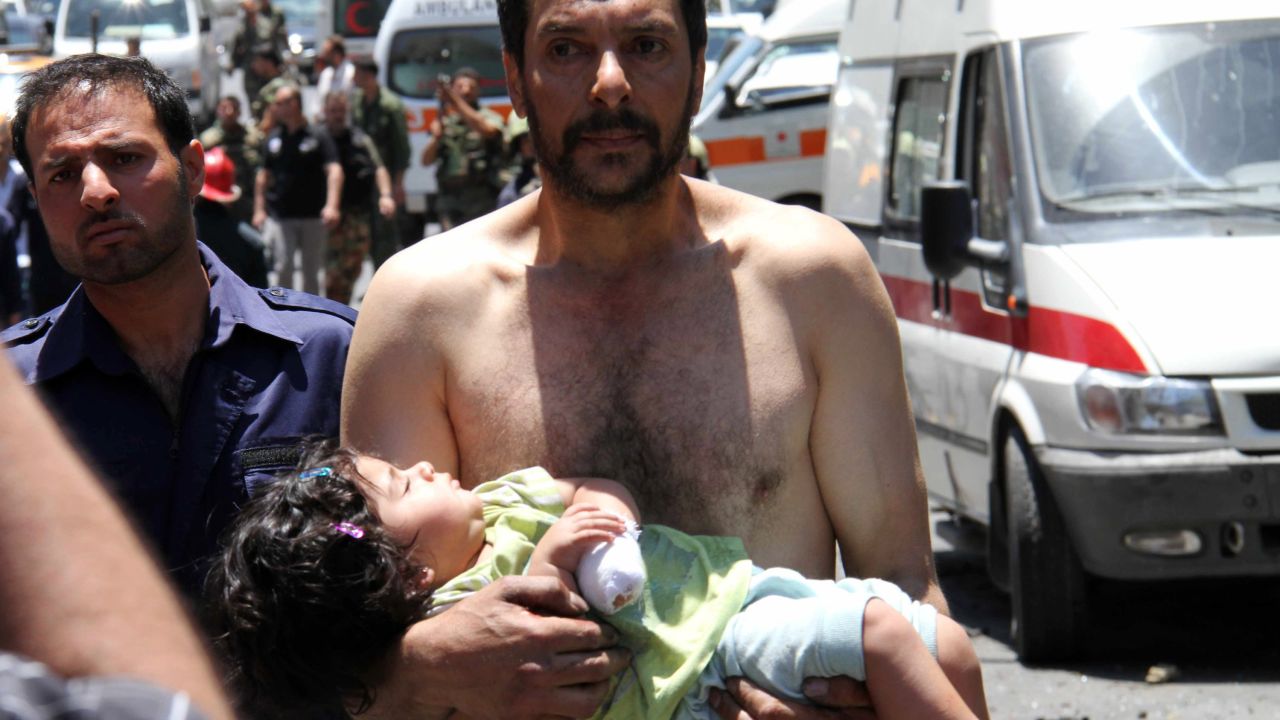 A Syrian man carries a wounded girl after an explosion targeted a military bus on June 8, 2012. 