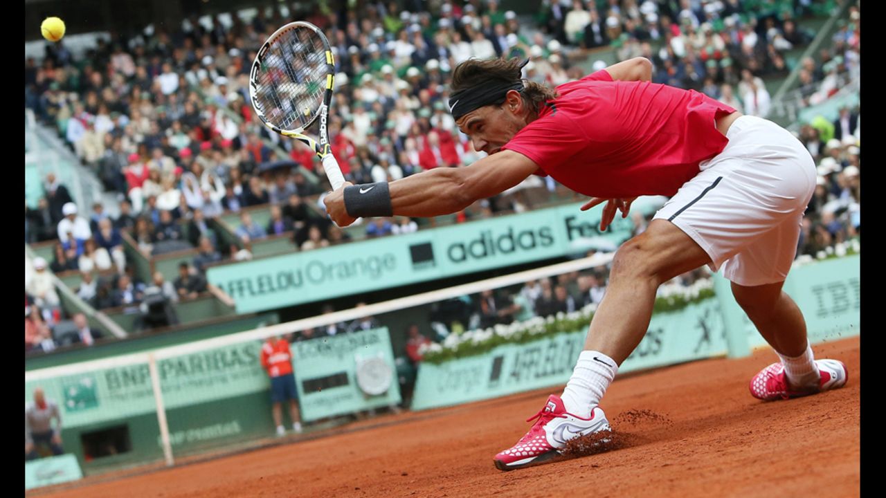 Nadal reaches and slides on the clay to return a ball from Djokovic.