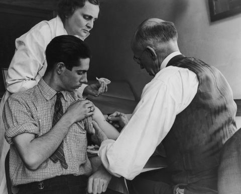 A teenage boy is vaccinated against smallpox by a doctor and a county health nurse in Gasport, New York, in  1938.