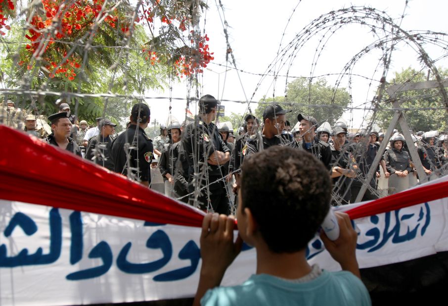 A boy peers through barbed wire at Egyptian military police standing guard outside the Constitutional Court in Cairo on Thursday, June 14.