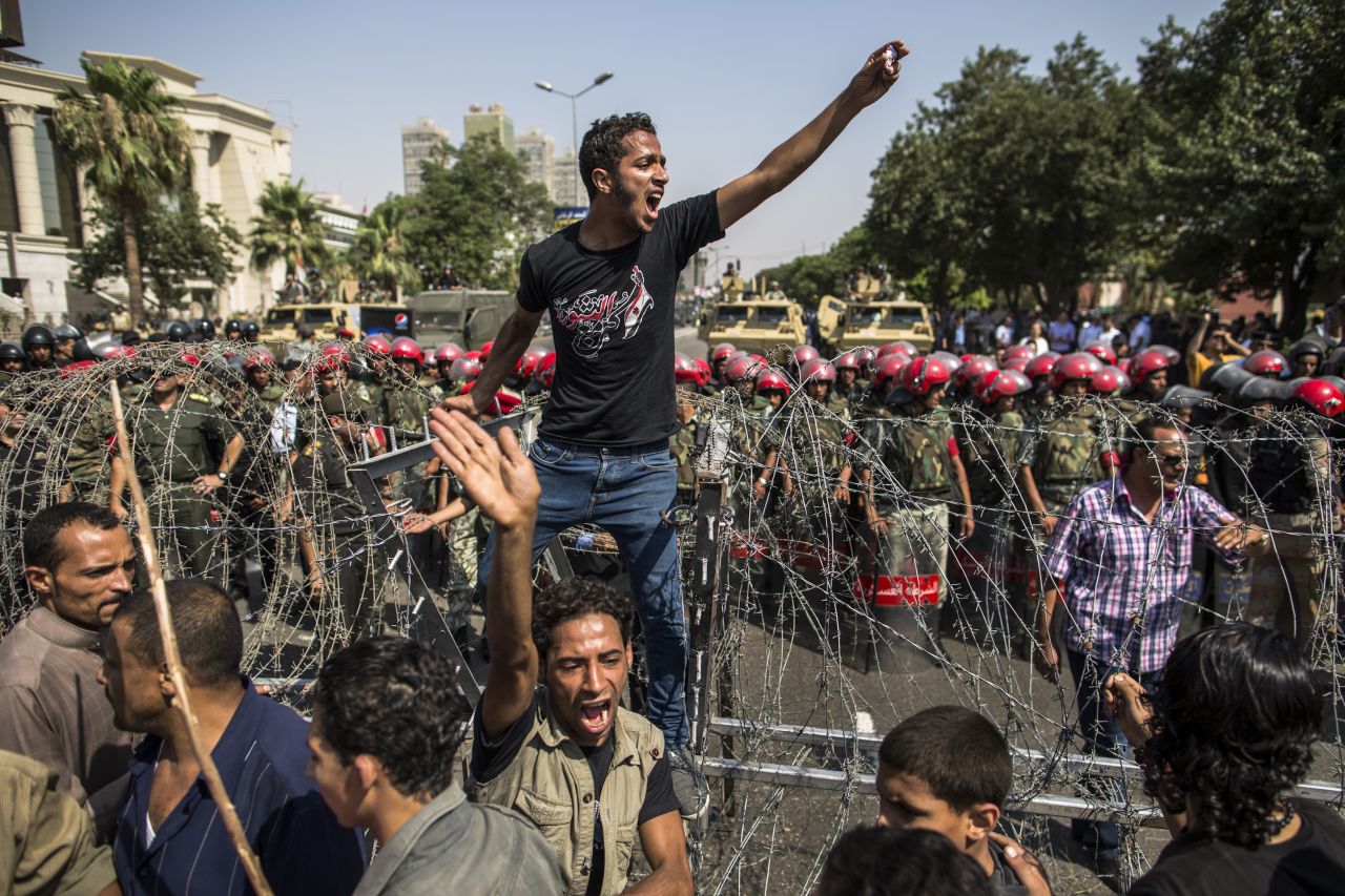 A protester stands on a barricade of barbed wire as Egyptian military police stand guard. Egypt's Supreme Constitutional Court ruled that the Islamist-led parliament must be immediately dissolved.