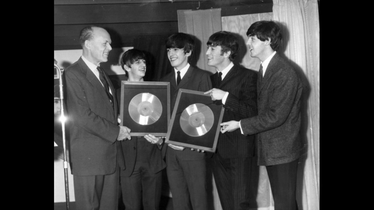 Sir Joseph Lockwood, chairman of EMI Music, presents The Beatles with two silver records for their albums "Please, Please Me" and "With The Beatles," which reached 250,000 sales.