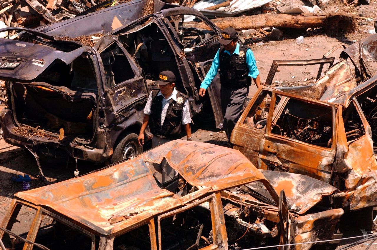 Indonesian police investigators walk through the wreckage of cars left twisted and burnt after the bomb attack in Bali. One witness, Nicolle Haigh, told police: "I've been told that there was about 45 seconds between explosions, but it felt like 10 seconds. One moment I was talking to friends, and the next was like being in a war zone."