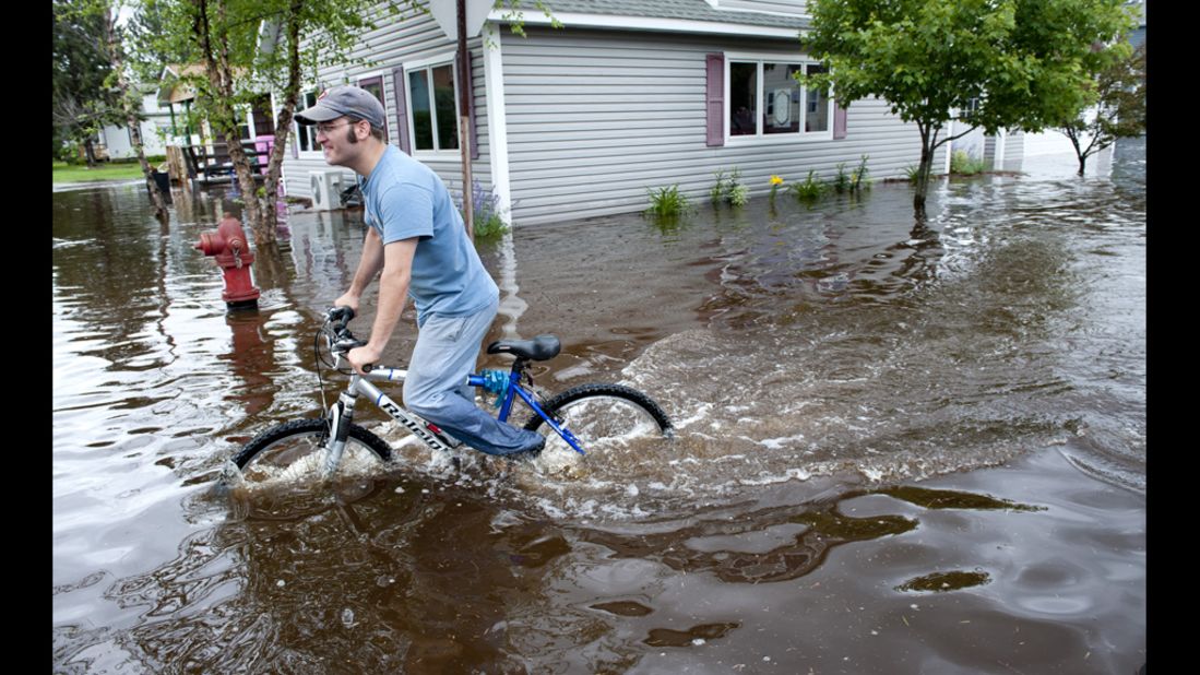 Brytton George rides a bike through flooded streets Wednesday near his home in Carlton. The flooding washed out roads and bridges, causing millions of dollars in damage.