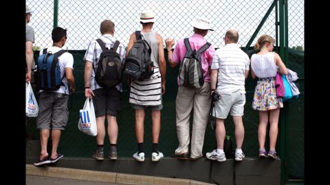 Fans peek through a fence to catch the action June 28 at Wimbledon.
