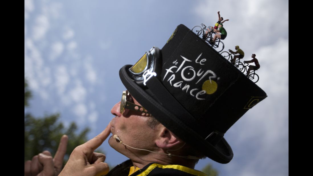 A performer wearing a hat decorated with toy cyclists poses for spectators on Saturday.