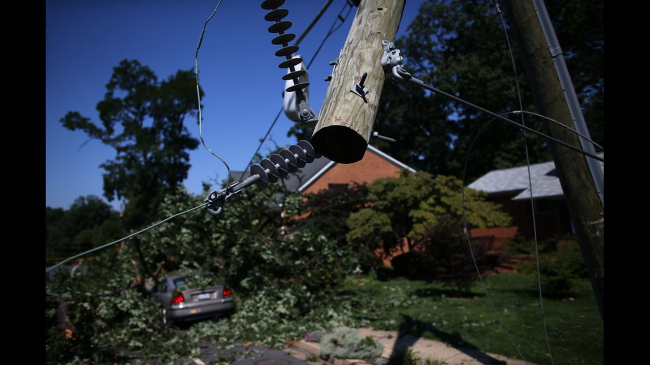 Power lines hang from a utility pole snapped in half and a fallen tree covers a car on Yorktown Boulevard in Arlington, Virginia.