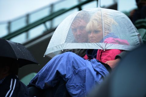 Spectators find shelter under an umbrella as they watch a match Monday.