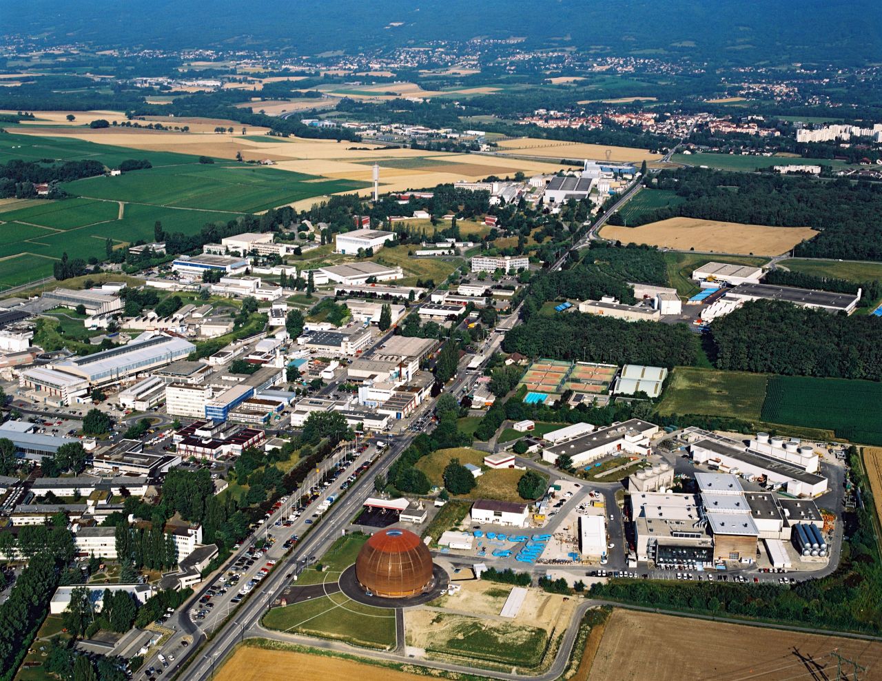 CERN's Globe of Science and Innovation exhibition centre and the nearby Meyrin site are seen from the air. The surface buildings which provide access and support for the ATLAS experiment, one of four experiments on the LHC, can also be seen on the right.