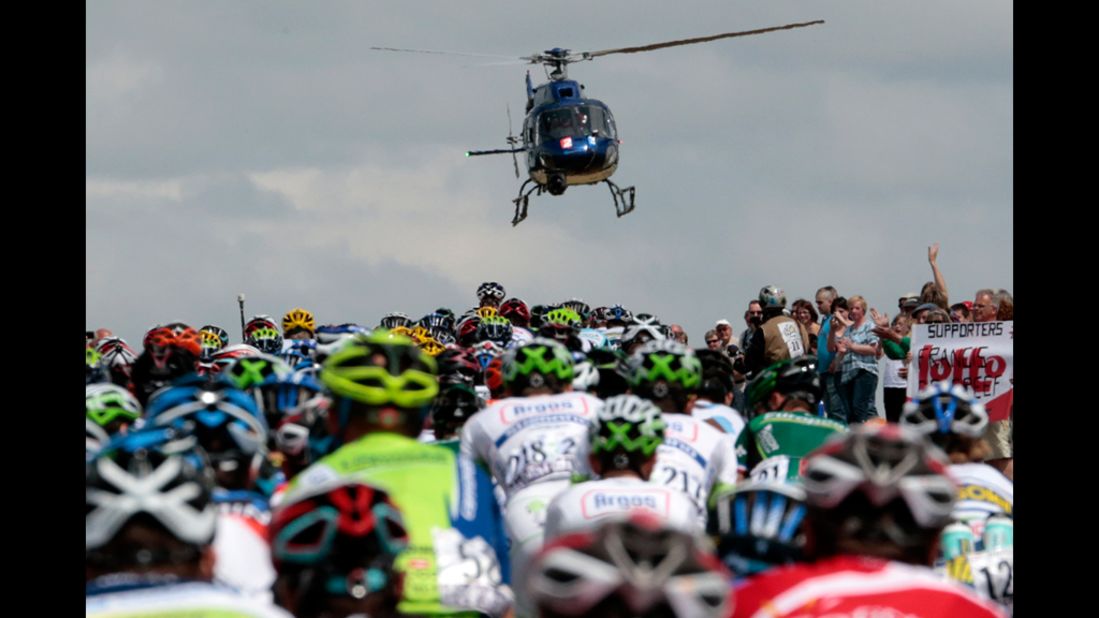 Fans cheer and a television helicopter flies above as the riders stream by.