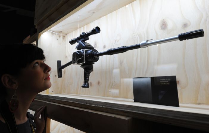 A woman poses for pictures next to a "Hasselblad Gun" used in the film "Licenced to Kill."