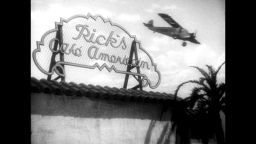 Full shot of plane flying over 'Rick's Cafe Americain' sign.