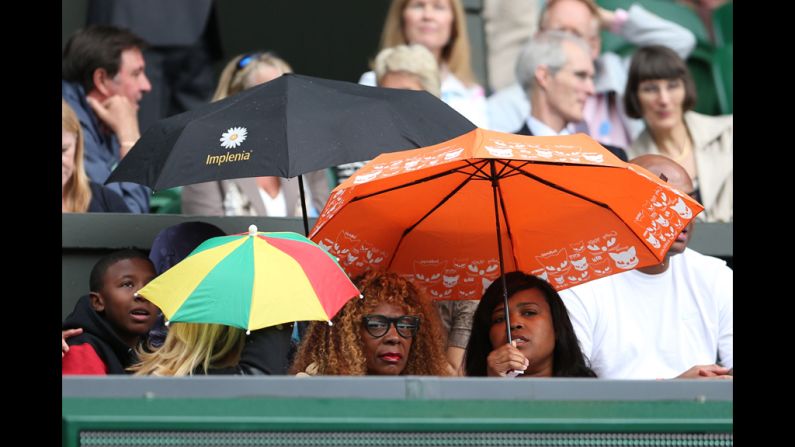 Williams' mother, Oracene Price, center, finds shelter under an umbrella during a temporary rain delay.