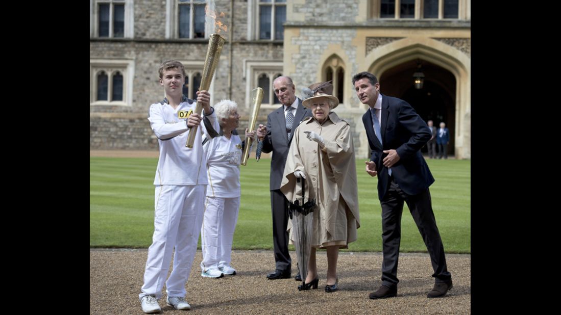 Prince Philip, Queen Elizabeth II and Lord Sebastian Coe watch as Olympic torchbearer Gina Macgregor passes the flame to Phil Wells at Windsor Castle in Windsor, England, on July 10.