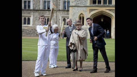 Prince Philip, Queen Elizabeth II and Lord Sebastian Coe watch as Olympic torchbearer Gina Macgregor passes the flame to Phil Wells at Windsor Castle in Windsor, England, on July 10.