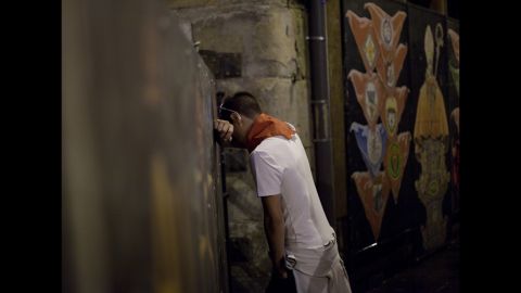 A reveler leans against the fence next to a painting of San Fermin in Curva Estafeta before Friday's running-of-the-bulls.