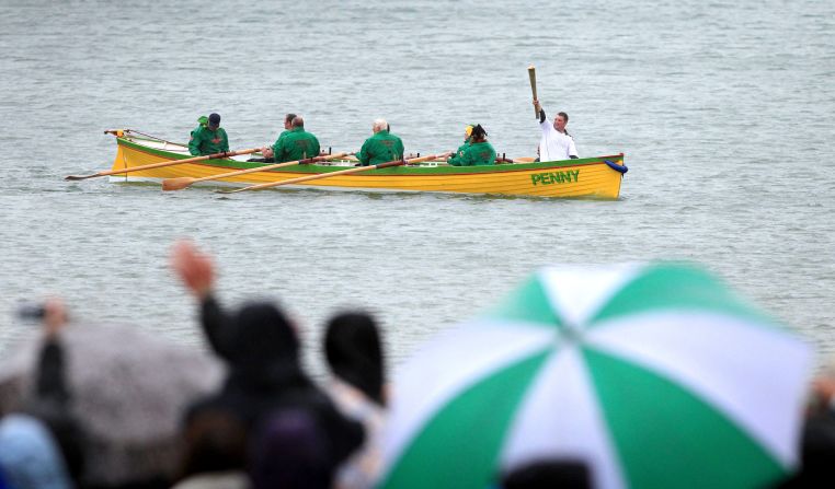 Ryan Hope carries the torch Thursday, July 12, on the row boat Penny off the waters of Weymouth.