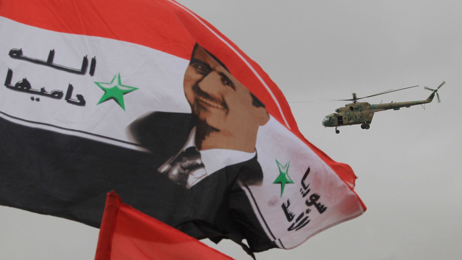 A Syrian army helicopter hovers above a national flag bearing a portrait of Syrian President Bashar al-Assad on January 11, 2012.