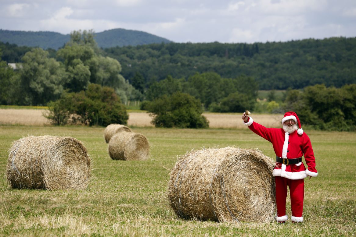 A spectator dressed as Santa Claus rings a bell from a field along the race route as riders pass by.