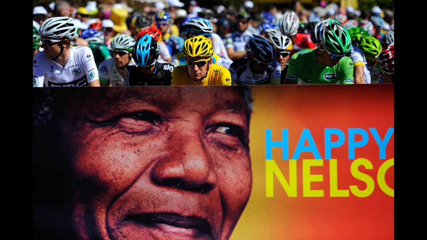 Race leader Bradley Wiggins of Great Britain, in yellow, and the main pack of riders pass a Nelson Mandela birthday banner Wednesday. People around the globe celebrated Mandela's 94th birthday.