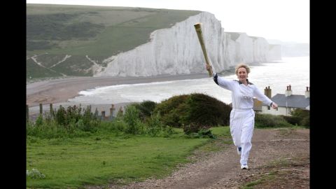Torchbearer Kathy Gore of Uckfield runs with the Olympic flame at Seaford Head in front of the Seven Sisters cliffs in East Sussex on Tuesday, July 17.
