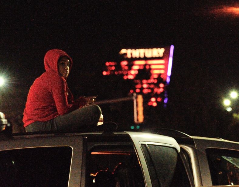 A woman sits on top of her car near the crime scene. 